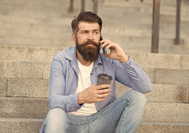 Modern urban life. Bearded man phone conversation. Mobile conversation. Coffee break. Personal communication. Calling friend. Pleasant conversation. Real connect. Drink coffee while talking - Фото, изображение