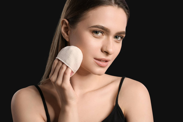 Beautiful young woman with makeup sponge on dark background - Photo, Image