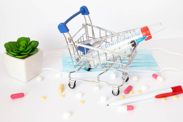 Shopping trolley and medicine. Expensive medicine. Shopping basket with blisters with pills and medicine bottles on a blue background. - Zdjęcie, obraz
