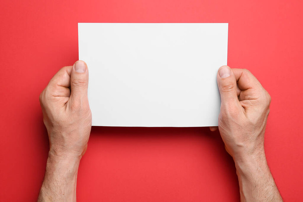 Hombre sosteniendo hoja en blanco de papel sobre fondo de color, primer plano - Foto, Imagen