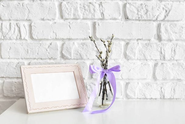 Willow branches with photo frame on table near brick wall - Foto, afbeelding