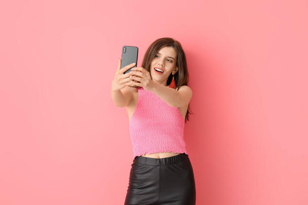 Κομψή νεαρή γυναίκα που παίρνει selfie στο φόντο χρώμα - Φωτογραφία, εικόνα