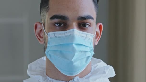 Portrait sad male face tired ethnic arabic hispanic doctor man medical worker surgeon specialist wear protective mask during pandemic corona in hospital looking at camera after complicated operation - Séquence, vidéo