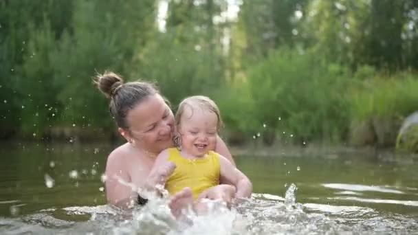 Kleine lustige süße blonde Mädchen Kleinkind im gelben Body lacht lernt draußen am Sommersee schwimmen. Plus Größe Körper positiv lächelnde Frau Mutter Baby Schwimmen in natürlichen Pool. Wasserspritzer. - Filmmaterial, Video