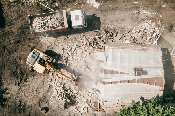 Excavator with bucket breaks house. Demolition of building, top view from drone - Photo, Image