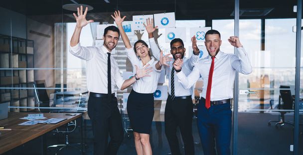 Portrait of satisfied male and female partners with raised hands satisfied with business triumph, excited diverse partners celebrating received opportunity with monetary gain posing in office - Photo, Image