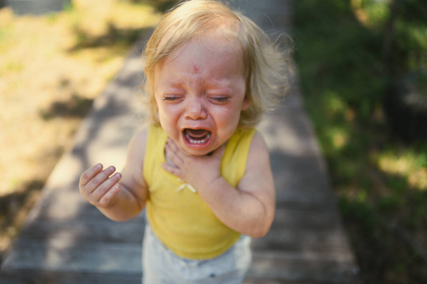 Detailní portrét malé zábavné roztomilé blondýny dítě batole ve žlutém obleku pláče venku v létě. Dětský záchvat vzteku. Zdravý koncept dětství. - Fotografie, Obrázek
