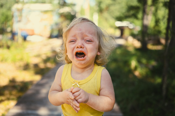 Κοντινό πορτρέτο του μικρού αστείο χαριτωμένο ξανθό κορίτσι παιδί νήπιο σε κίτρινο κοστούμι του σώματος κλαίει έξω το καλοκαίρι. Παιδικό ξέσπασμα. Υγιής έννοια παιδική ηλικία. - Φωτογραφία, εικόνα