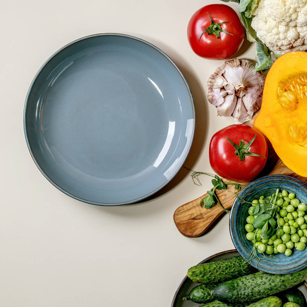 Variety of fresh raw organic vegetables for cooking. Half of hokkaido pumpkin, young green pea, cauliflower, cucumbers and empty plate over beige background. Healthy eating concept. Flat lay, space. Square - Foto, imagen