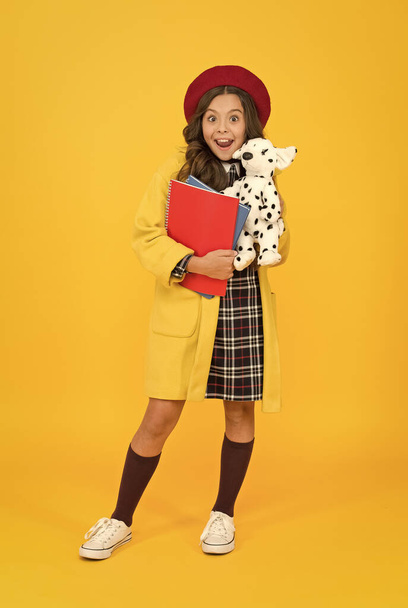 education concept. childhood happiness. school and fashion. child in pupil uniform. kid in french beret on yellow background. stylish teen college student. little girl with toy dog and notebooks - Fotografie, Obrázek