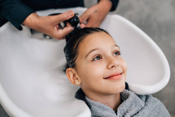 Young girl enjoying at hairstyle treatment while professional hairdresser gently washing her hair. - 写真・画像
