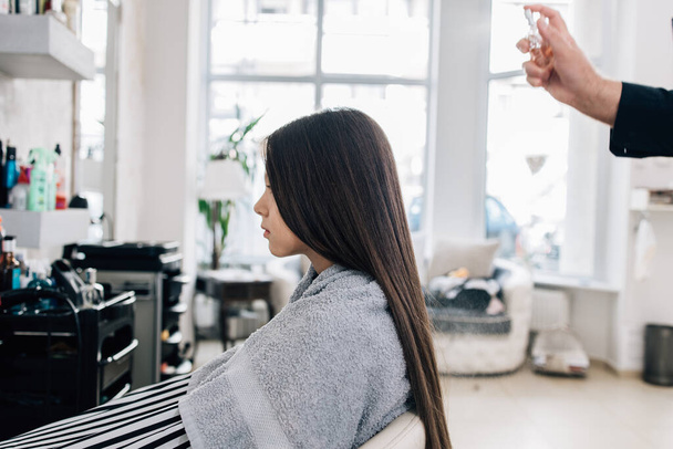 Νεαρό κορίτσι απολαμβάνει τη θεραπεία hairstyle, ενώ η επαγγελματίας κομμώτρια εργάζεται απαλά και κόβοντας τα μαλλιά της. - Φωτογραφία, εικόνα