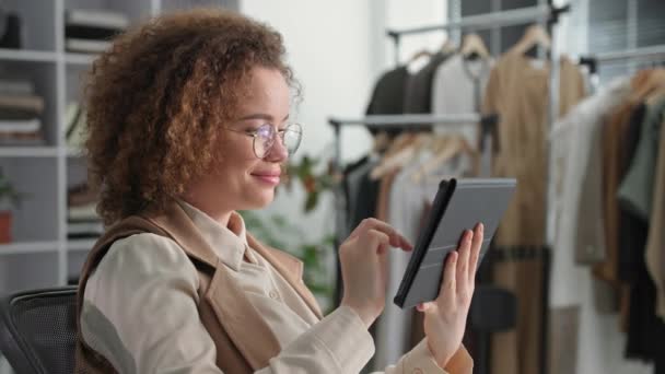 portrait of a charming girl working in a clothing store and texting with a customer online using modern tablet technology in an internet boutique - Footage, Video