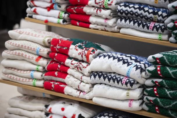 Є стопки в'язаних светрів з різдвяним візерунком на полиці магазину. Новорічний розпродаж
. - Фото, зображення