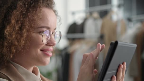 portrait of a female seller wearing glasses uses social media to sell clothes online while sitting in a fashion store - Footage, Video