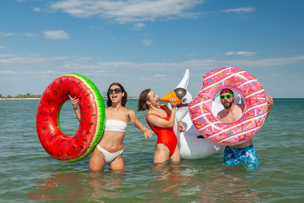two young women and a man on rubber rings in the sea in the summer - Foto, Imagen