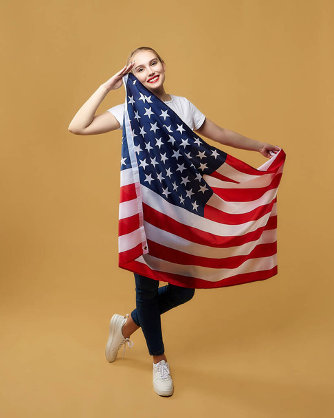 atrakcyjna blondynka z dumą pozuje z amerykańską flagą. sesja zdjęciowa w studio na żółtym tle. - Zdjęcie, obraz