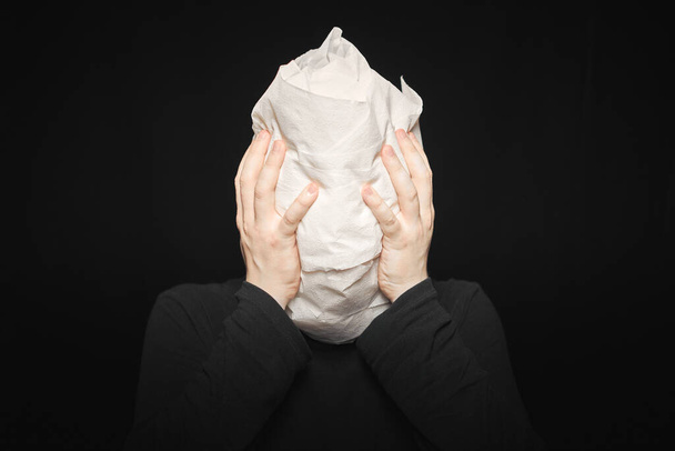 Head wrapped in toilet paper. Man holds his hands behind his head. Funny man, black background. Mummy, mental health concept. Oh my god. - Foto, imagen