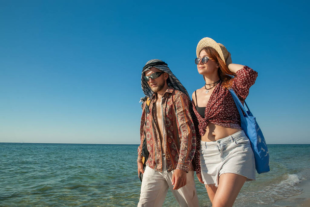 a man with a woman in hats and sunglasses are walking along the seashore in the summer - Photo, Image