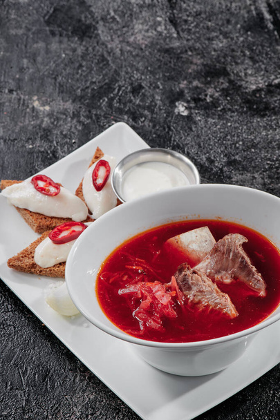 自家製ロシア、ウクライナ、ポーランドの国民のスープ-ビートルート、野菜や肉で作られた赤いボルシチサワークリーム。テクスチャ暗い背景で  - 写真・画像