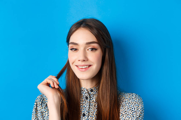 Lähikuva muotokuva flirttaileva nuori nainen luonnon kauneutta, hymyilee ja leikkii hiukset Strand, joilla on mielenkiintoinen idea, seisoo sinisellä pohjalla - Valokuva, kuva