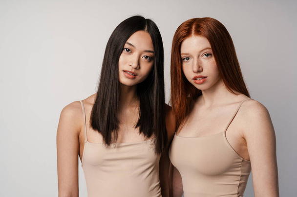 Multiracial two women posing and looking at camera isolated over white wall - Foto, Bild