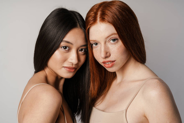 Multiracial two women posing and looking at camera isolated over white wall - Foto, Bild