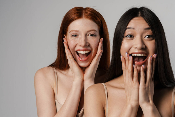 Close up studio portrait of two excited beautiful young girls with clear fresh young face skin posing over white wall, looking at camera - Valokuva, kuva