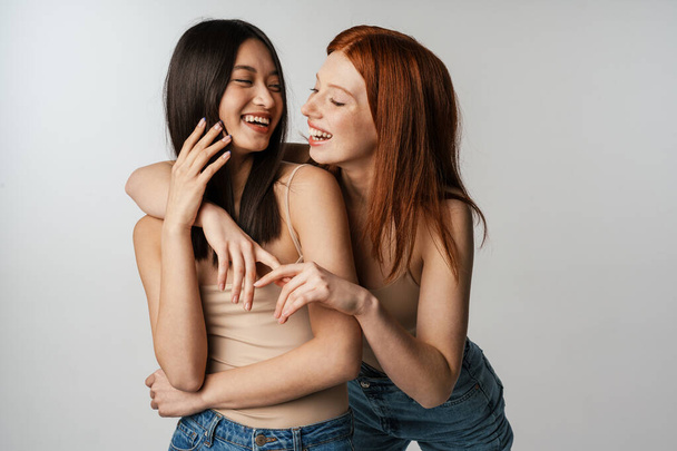 Multiracial two women hugging and laughing at camera isolated over white wall - Фото, зображення