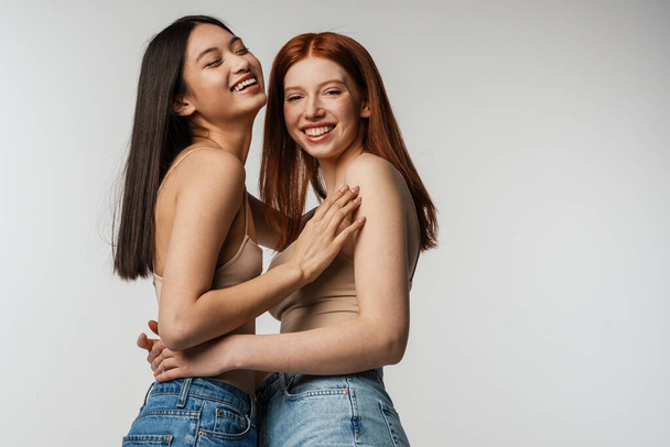 Multiracial two women hugging and laughing at camera isolated over white wall - Φωτογραφία, εικόνα
