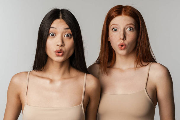 Multiracial two women expressing surprise at camera isolated over white wall - Foto, Imagen