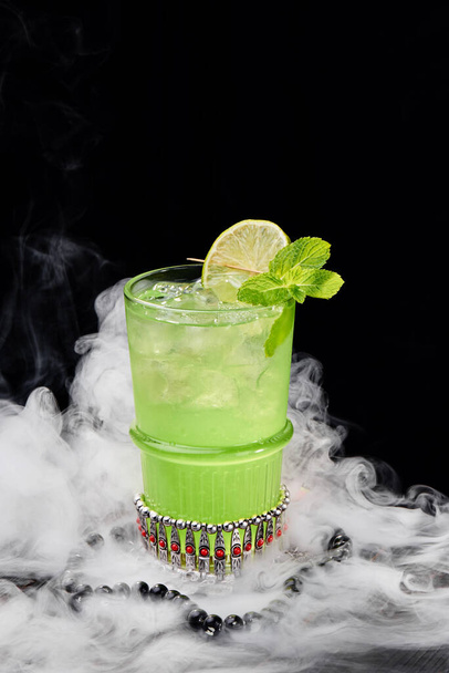 Mint green cocktail with ice in glass on a black background with smoke. Space for text - Fotografie, Obrázek