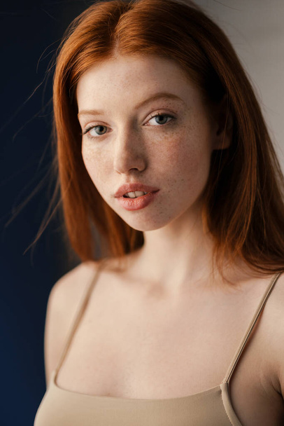 Close up of a young red haired woman posing indoors, looking at camera - 写真・画像