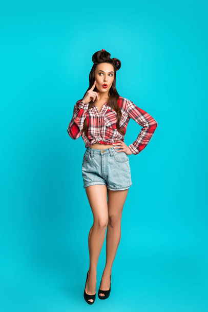 Surprised pinup woman in retro style clothes cannot believe great offer or huge sale over blue studio background - Foto, immagini