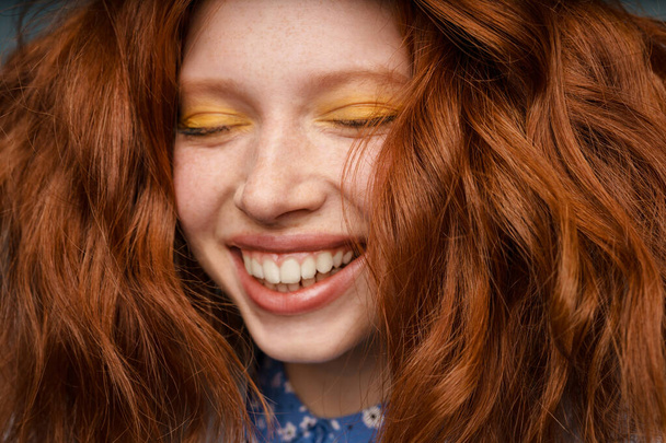 Young ginger joyful woman laughing with eyes closed indoors - 写真・画像
