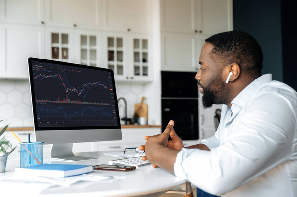 Investments, trading on the stock exchange. African american man trader investor, is analysing cryptocurrency financial market, looks at computer,trading data index chart graph on pc screen - Fotografie, Obrázek