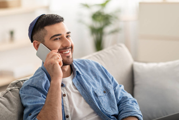 Uśmiechnięty tysiącletni mężczyzna rozmawiający przez telefon w domu - Zdjęcie, obraz