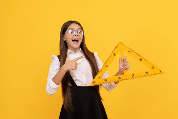 niño sorprendido en uniforme escolar y gafas sostienen triángulo matemático para medir, trigonometría - Foto, Imagen