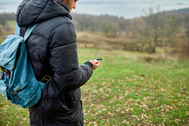 Homem viajante com mochila com bússola na mão em um fundo de montanhas rio da natureza, conceito de viagem, camping viagem, GPS, orientação, navegador - Foto, Imagem