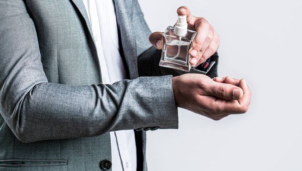 Fragrance smell. Men perfumes. Fashion cologne bottle. Man holding up bottle of perfume. Men perfume in the hand on suit background. Man in formal suit, bottle of perfume, closeup - Фото, зображення