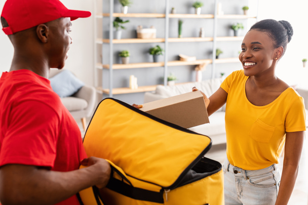 koerier geeft doos aan zwarte dame leveren bestelling aan deuren - Foto, afbeelding