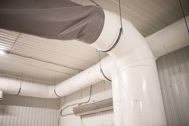 Ventilační potrubí ve skladišti. komunikace pro oběh čerstvého vzduchu v průmyslových prostorách. pod stropem jsou natažené bílé kovové trubky. ventilační a chladicí systém - Fotografie, Obrázek