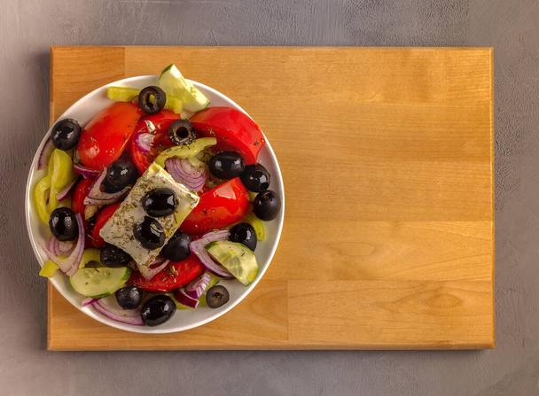 Ελληνική χωριάτικη σαλάτα σε λευκό πιάτο που στέκεται πάνω σε ξύλινη σανίδα. Αντιγραφή χώρου. - Φωτογραφία, εικόνα