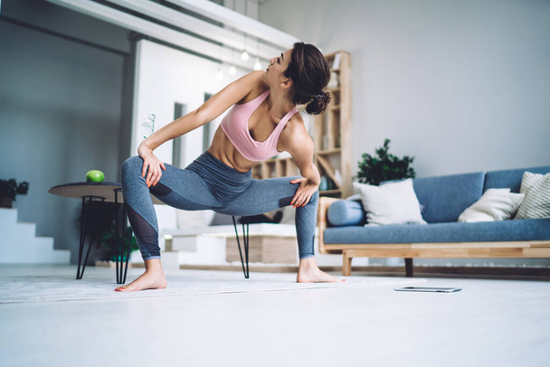 Strong Caucasian woman in casual wear stretching body muscles and recreating during morning yoga practice, flexible calm female enjoying healthy lifestyle during active pilates at home interior - Foto, Imagen