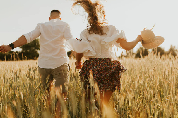 L'esprit de voyage, de liberté et d'indépendance. Joyeux jeune couple amoureux courant dans les champs au coucher du soleil. Cheveux sales. Concept de liberté et d'amour. Gros plan sur la prise de main. - Photo, image