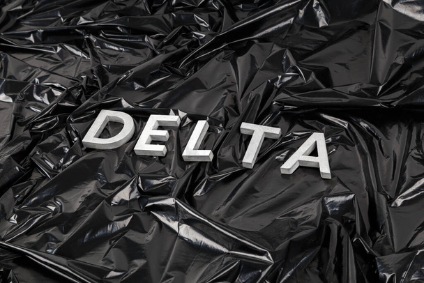 слово дельта укладывается с серебряными металлическими буквами на скомканном черном пластиковом фоне в диагональной перспективе - Фото, изображение