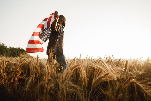 African american young man holding USA national flag through wheat field - Fotó, kép