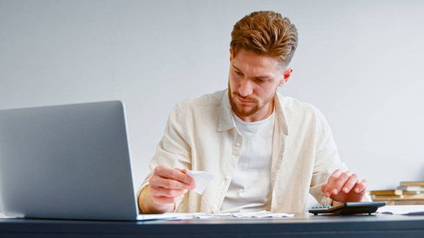 Skilled accountant looks at paper checks and summarizes total on calculator sitting at table - Foto, Bild