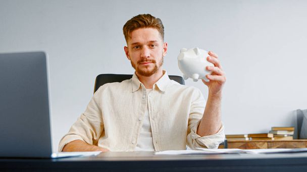 Serieuze man corporate bedrijfsleider met baard houdt witte spaarpot - Foto, afbeelding