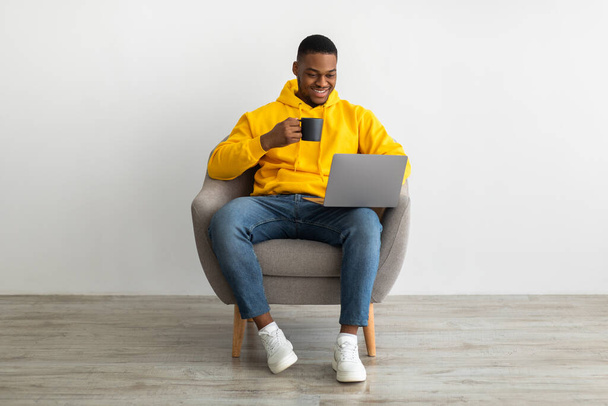 alegre preto homem trabalhando no laptop beber café sentado dentro de casa - Foto, Imagem
